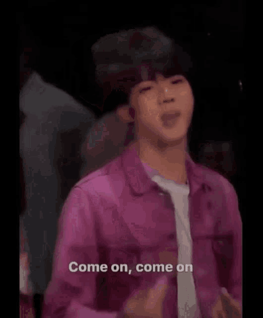 a man in a pink jacket is standing in front of a crowd and says come on come on .