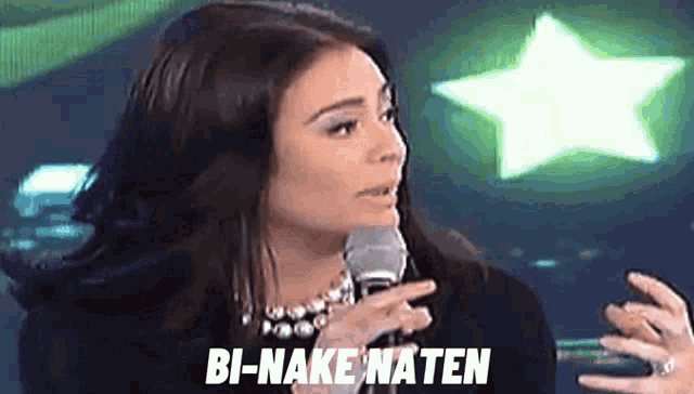 a woman is talking into a microphone and the words bi-nake naten are on the screen behind her .