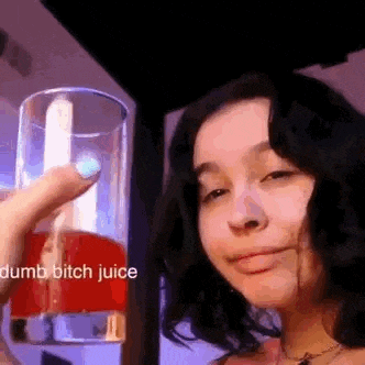 a woman is holding a glass of red juice and smiling .
