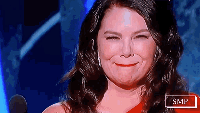 a woman in a red dress smiles in front of a microphone with smp written on the bottom