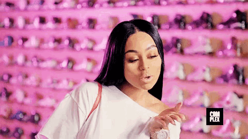 a woman in a white shirt is standing in front of a pink wall of shoes .
