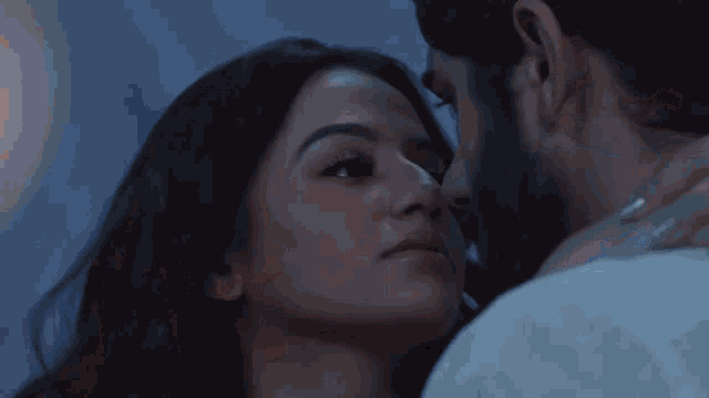 a man and a woman are kissing in a dark room with a candle in the background .