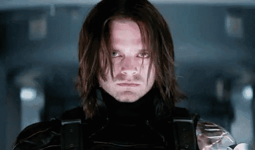 a close up of a man with long hair wearing a black suit and a turtleneck .