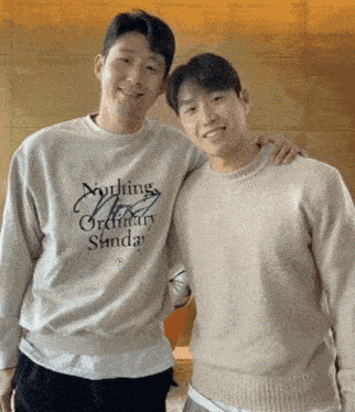 a man wearing a sweater that says nothing ordinary sunday stands next to another man