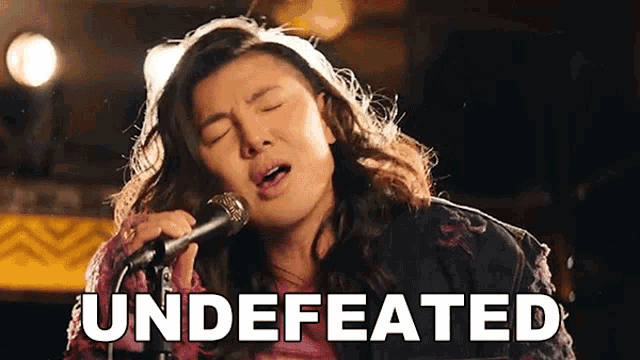 a woman singing into a microphone with the words " undefeated " above her