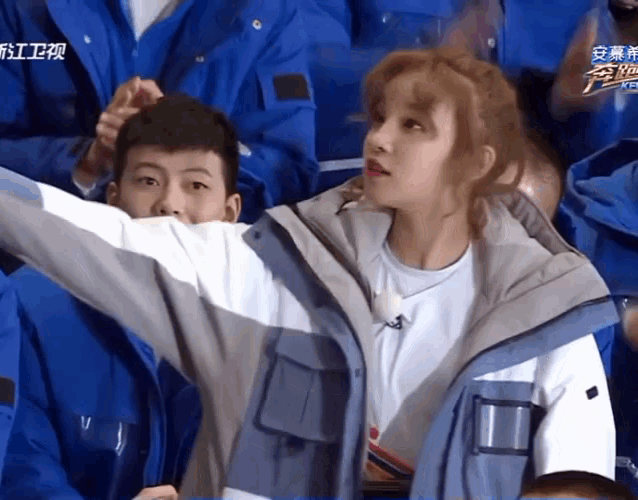 a group of people in blue jackets are sitting in a stadium with chinese writing on the screen