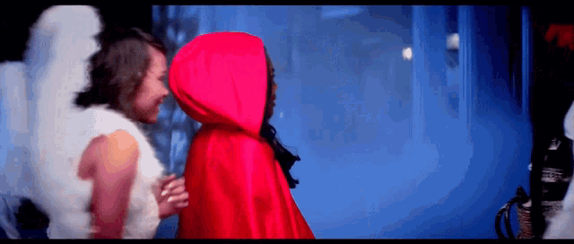 a woman in a red cape talks to a woman in an angel costume