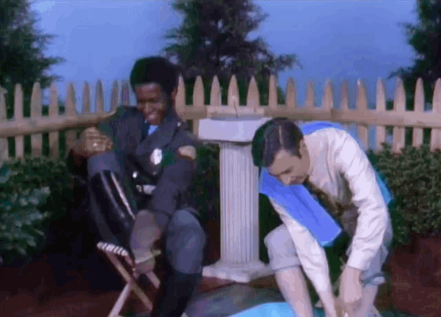 a man in a blue cape sits next to a man in a white shirt