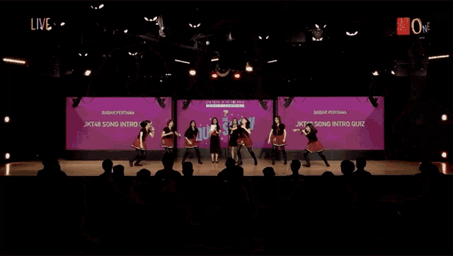 a group of girls are standing in front of a purple wall with the word live on it