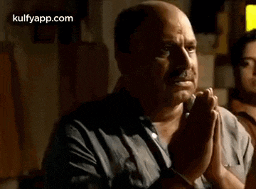 a bald man is praying with his hands folded in front of him .
