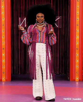 a woman with a large afro is standing on a stage wearing a purple shirt and white pants .