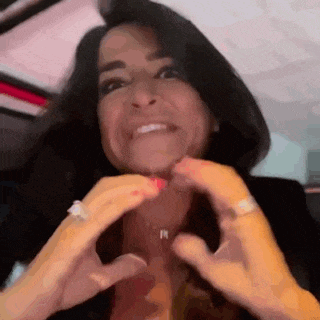 a woman is smiling and making a heart shape with her hands .
