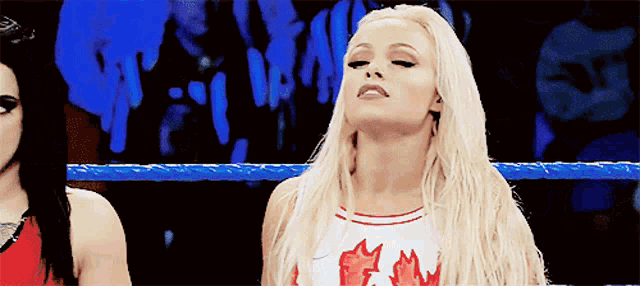 a blonde woman wearing a red and white top with a maple leaf on it stands in a wrestling ring