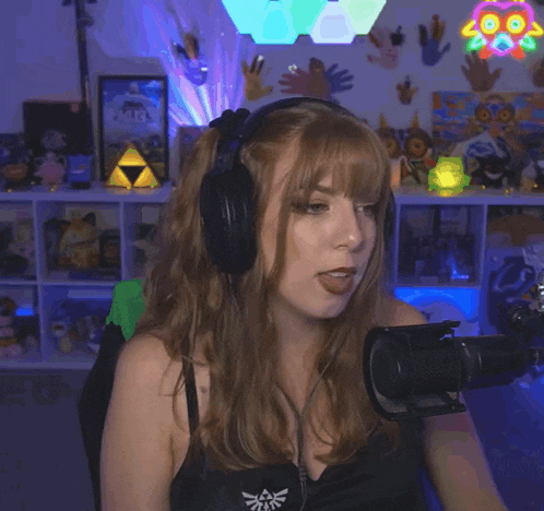 a woman wearing headphones stands in front of a microphone with a zelda logo on her shirt