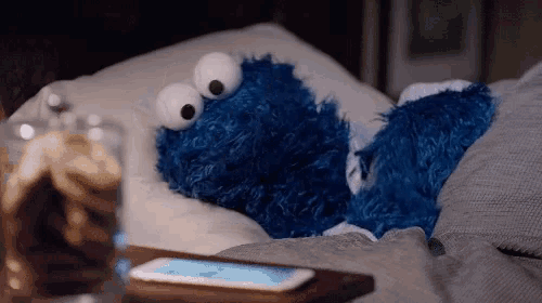 a cookie monster laying on a bed next to a phone