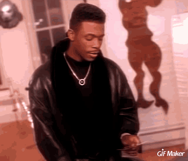a man wearing a black leather jacket and a necklace with a gif maker logo on the bottom