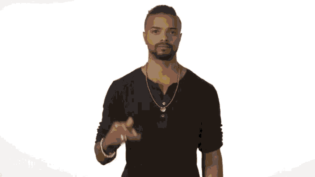 a man in a black shirt and gold chain is throwing a bottle of beer in the air .