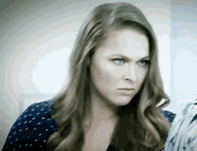 a woman with long hair and blue eyes is making a serious face .