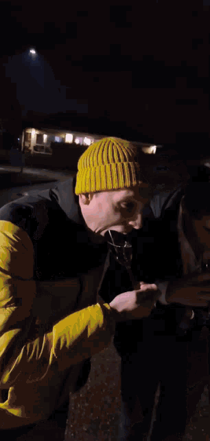 a man wearing a yellow beanie is holding a spoon in his mouth