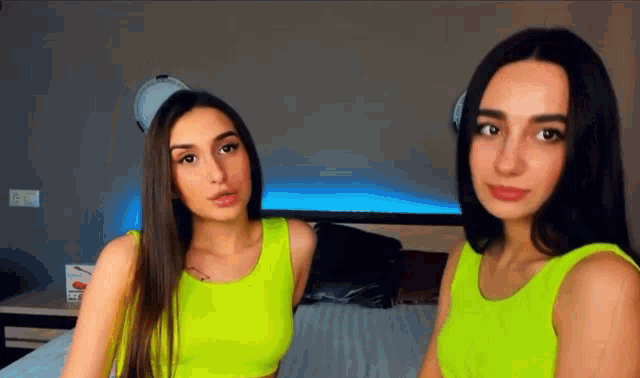 two women in neon green tank tops are standing next to each other on a bed .