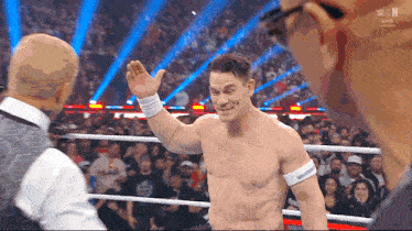 a shirtless wrestler in a wrestling ring waves to a crowd