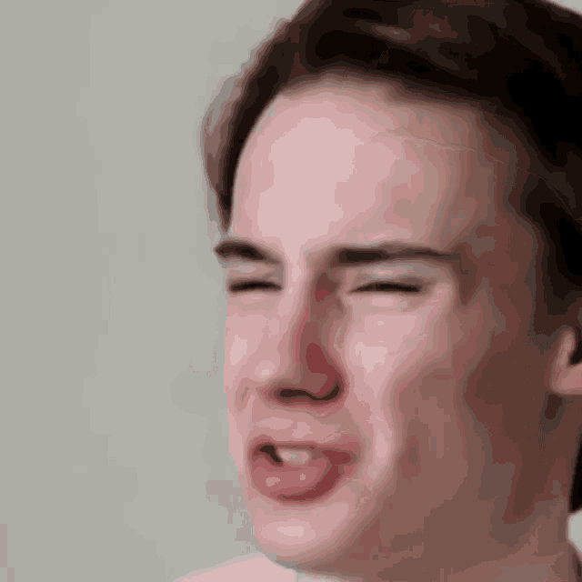 a close up of a young man making a funny face with his eyes closed and his tongue out .