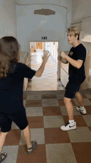 two boys are standing in a hallway and one has a nike logo on his shirt