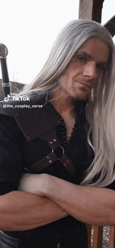 a man with long white hair and a beard is standing next to a woman with her arms crossed ..