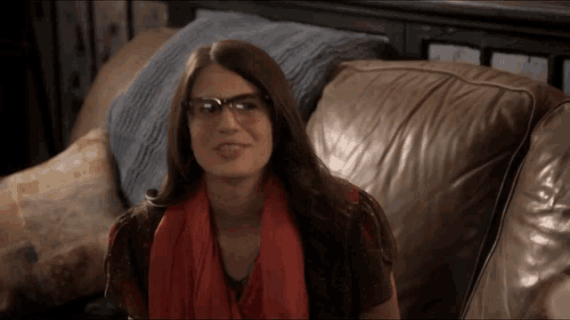 a woman wearing glasses and a red scarf is sitting on a couch