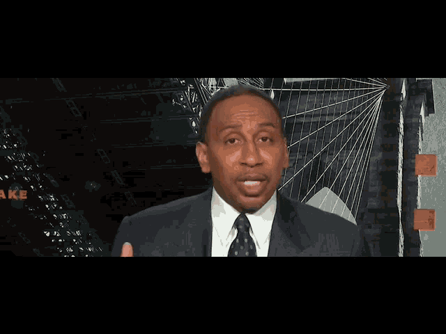 a man in a suit and tie is talking in front of a sign that says make