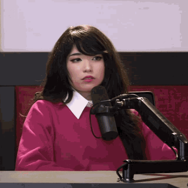 a woman in a pink sweater sits in front of a black microphone