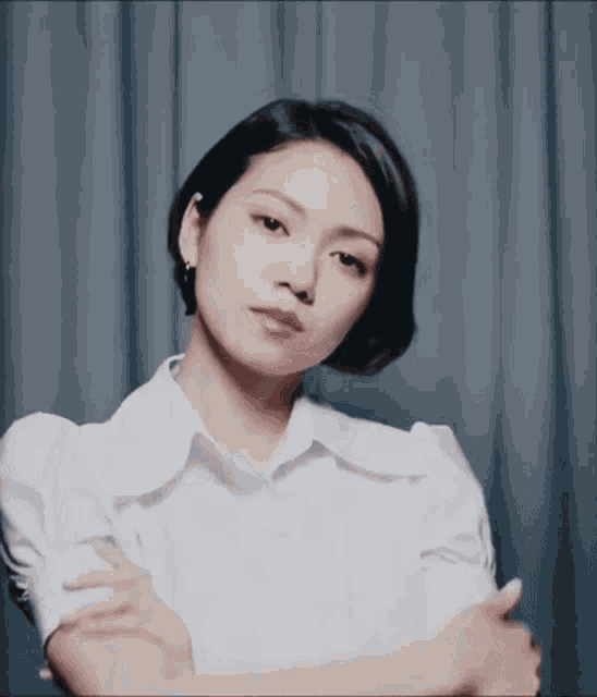 a woman wearing a white shirt with her arms crossed looks at the camera