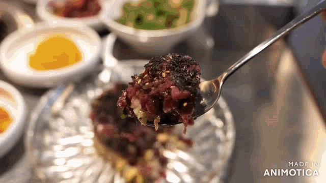 a person is holding a spoon with a piece of food on it in front of a glass plate .