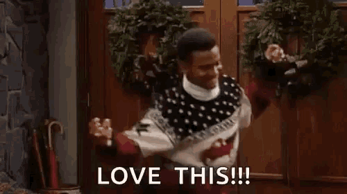 a man in a sweater is standing in front of a door with a wreath on it and says `` love this '' .