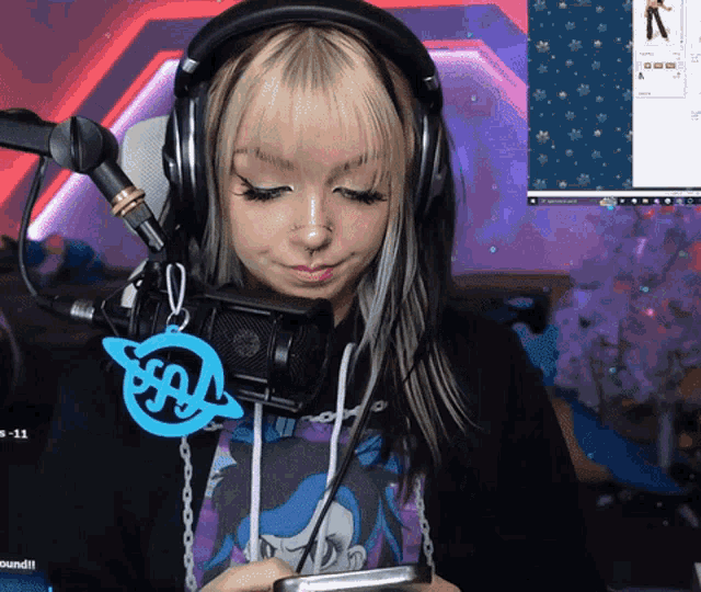 a woman wearing headphones and a keychain with the letter r on it is looking at her phone