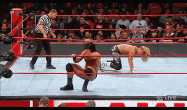 two wrestlers in a wrestling ring with a referee and a sign that says live
