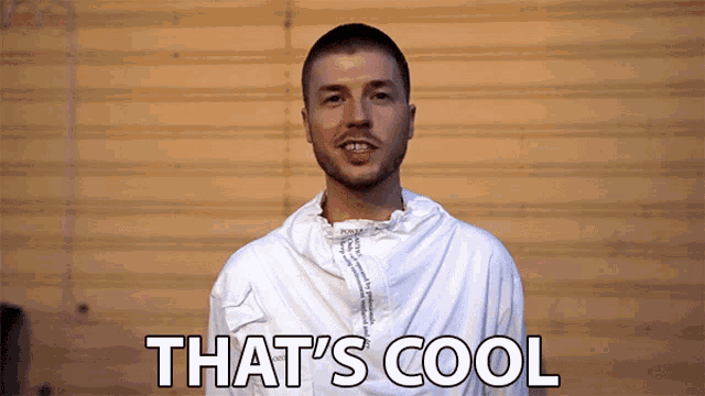 a man in a white jacket says that 's cool in front of a wall