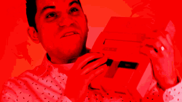 a man in a red shirt is holding a nintendo entertainment system in his hands