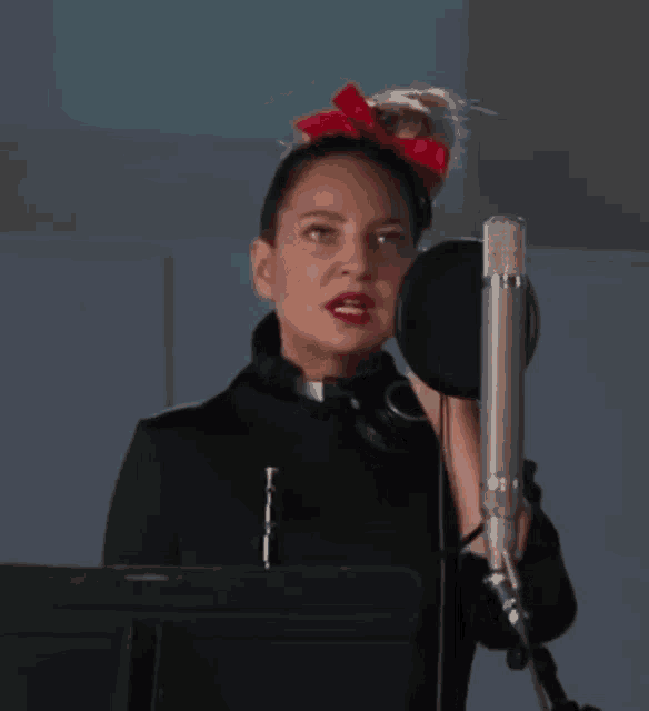 a woman wearing headphones and a red bow in her hair sings into a microphone