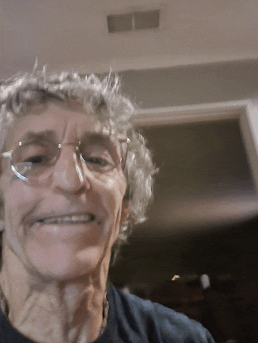 a man with curly hair wearing glasses is smiling for the camera