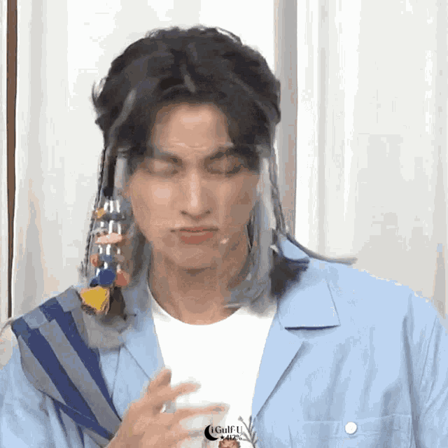 a man with long hair is making a funny face while holding a glass of water .