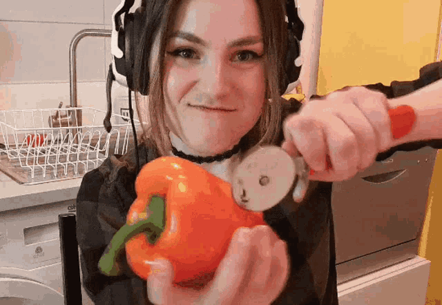 a woman wearing headphones is holding an orange pepper and a pizza cutter