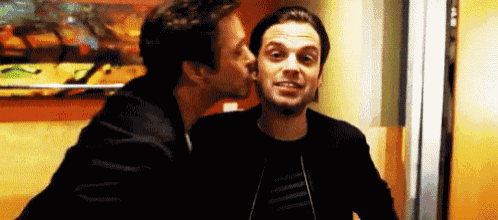 a man is kissing another man on the cheek while standing next to each other .