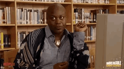 a bald man is sitting at a desk in front of a computer in a library .
