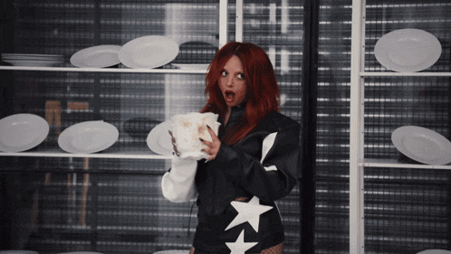 a woman with red hair is holding a piece of paper in front of a shelf of plates