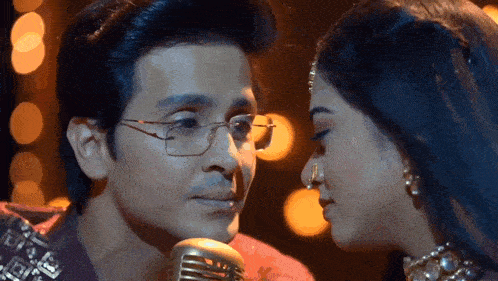 a man and woman are kissing in front of a microphone . the man is wearing glasses .