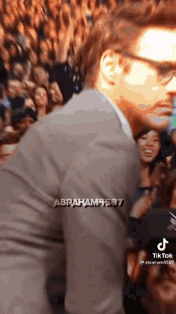 a man in a suit and glasses is standing in front of a crowd .