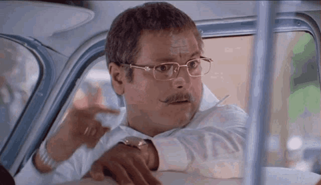 a man with glasses and a mustache is sitting in a car and pointing