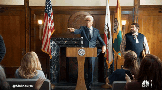 a man stands at a podium giving a speech with the hashtag #mrmayor visible