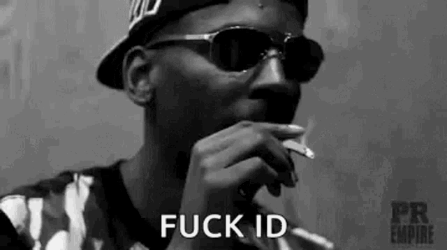 a black and white photo of a man wearing sunglasses and a hat smoking a cigarette .